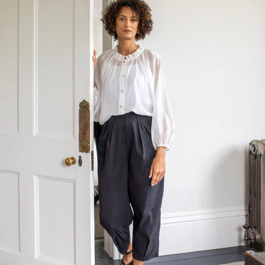Woman standing in a doorway wearing a white blouse and black pants.