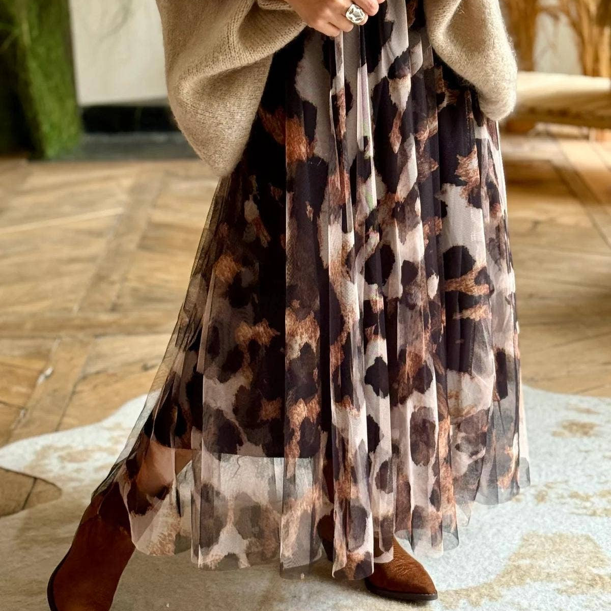 Person wearing a beige sweater and leopard print skirt on a wooden floor.
