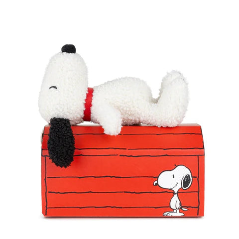Plush toy of a dog lying on a red bench with black lines, resembling a famous comic strip character.