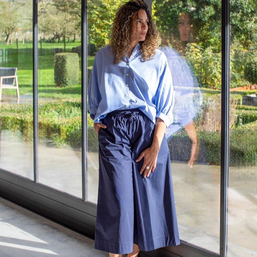 A person standing by a window wearing navy wide leg cotton culottes with a drawstring waist.